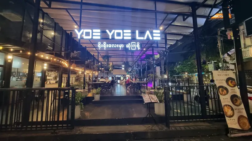 Yoe Yoe Lae Pratunam at night: the lit sign over an open terrace strung with lights.
