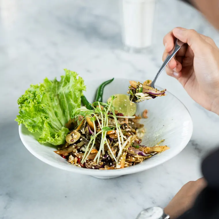 A tea-leaf salad being eaten with a fork, on a marble table.